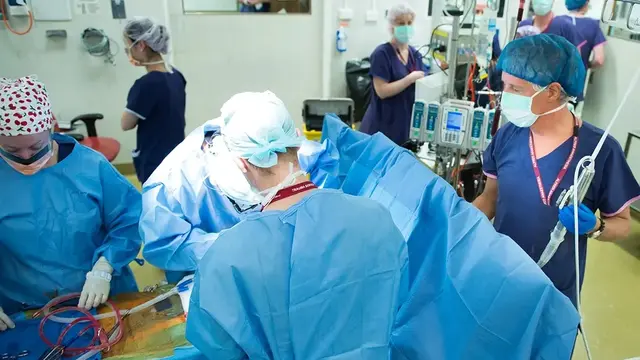 A surgical team performs a procedure in a high-intensity operating room, representing research into perioperative fluid management and its impact on patient recovery.