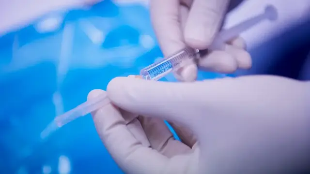 Gloved hands holding needle with liquid inside