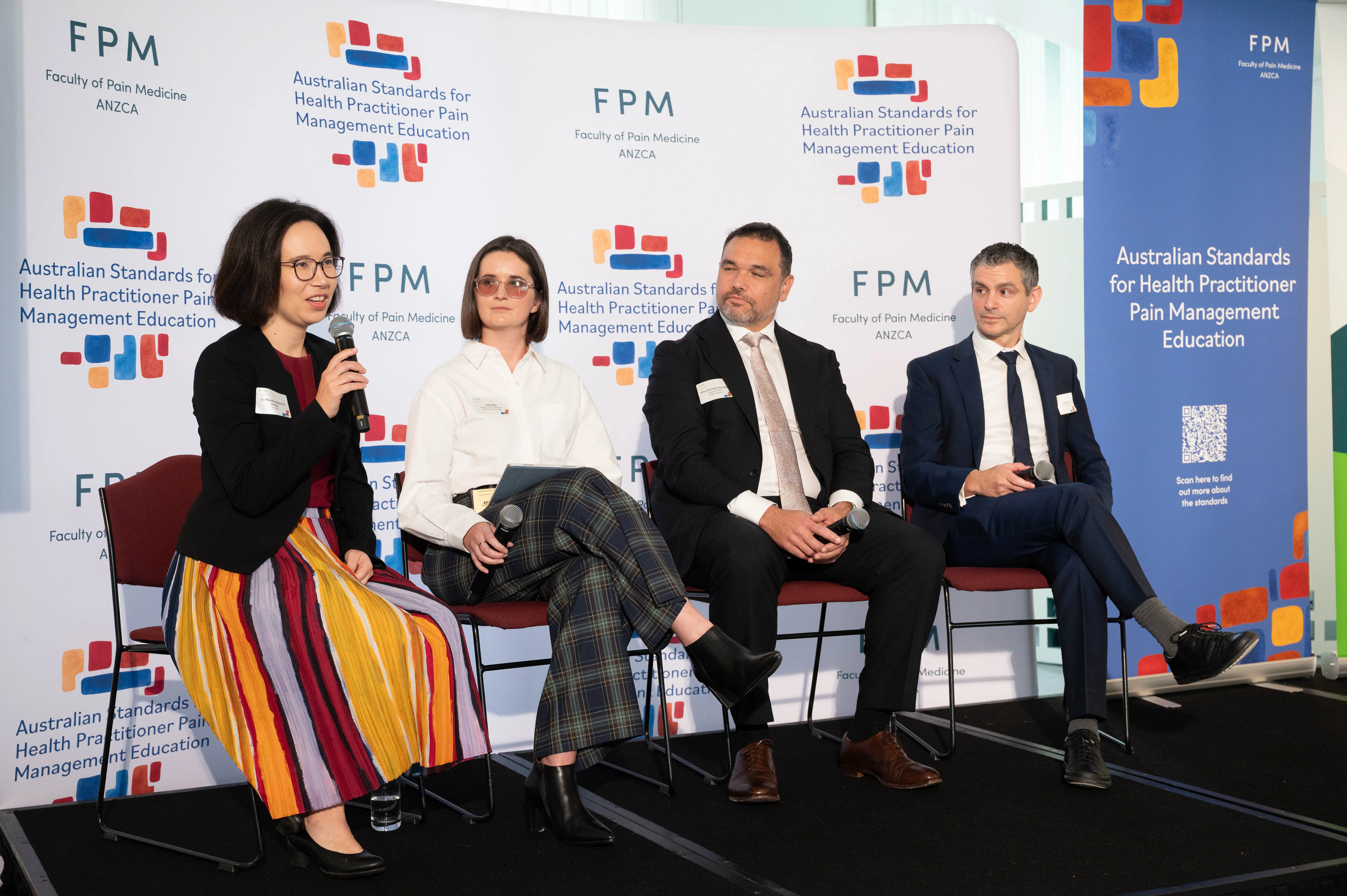 A photo of a speaking panel in front of an FPM and Education standards media wall