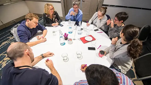 A group of professionals engaged in a discussion around a table, taking notes and collaborating in a meeting setting