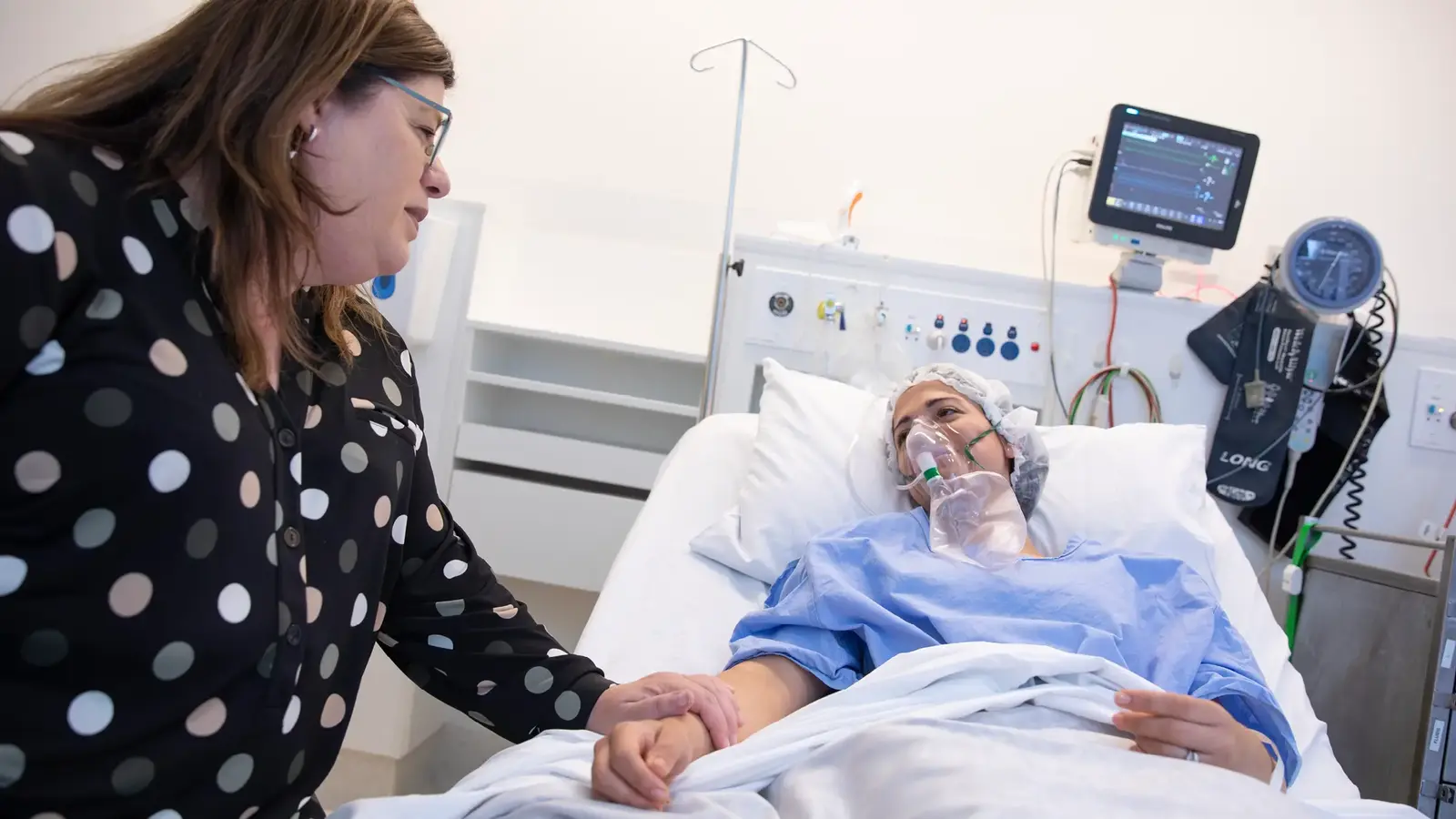 Person comforting patient in hospital bed