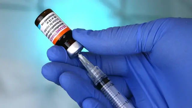 A gloved healthcare professional draws Dexamethasone from a vial into a syringe against a cool-toned, clinical background.