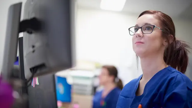 Person in scrubs and wearing glasses looking at computer screen