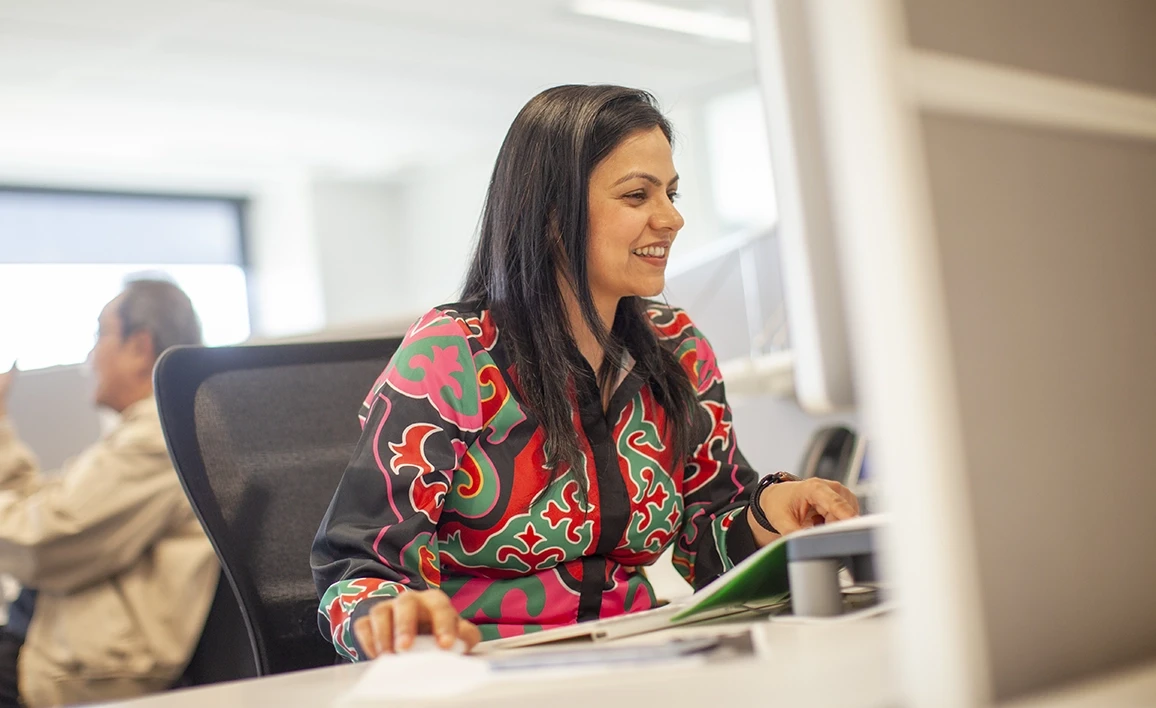 A research coordinator is sitting at a computer desk doing an online course in a brightly lit office space.