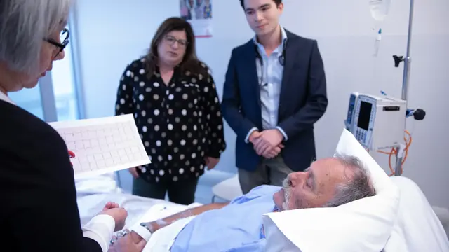 Three doctor's review an older male patient at a hospital bedside