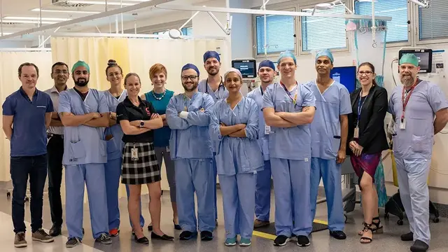 A diverse team of healthcare professionals, including surgeons, nurses, and administrators, pose together in a hospital setting, dressed in scrubs and professional attire.