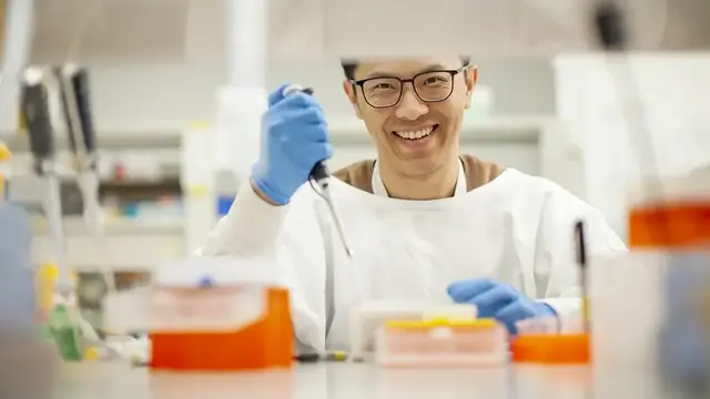 A researcher in a laboratory setting smiles while using a pipette, highlighting enthusiasm and innovation in scientific research.