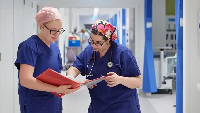 Two female doctor's looking at a chart in a hospital corridor
