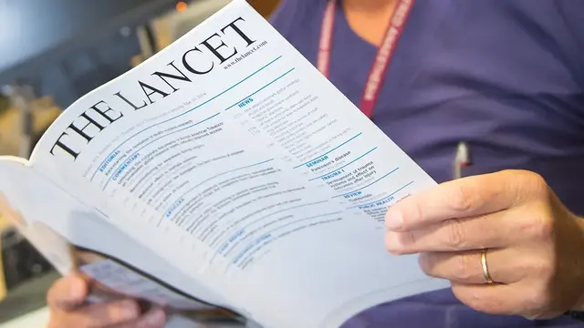 An anaesthetist in medical attire reading The Lancet, a well-known medical journal, reviewing published trial results