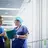 Two people in blue scrubs talking in a hospital corridor. One is holding a folder of papers