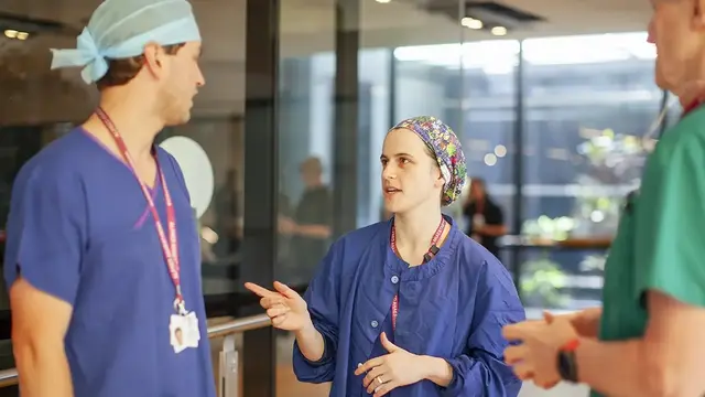 Three healthcare professionals in scrubs having a discussion in a hospital setting.