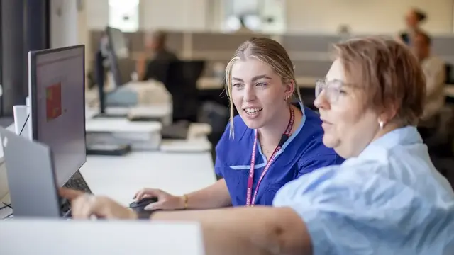 Two research coordinators collaborate at a computer, discussing data analysis and project management in a clinical research setting.