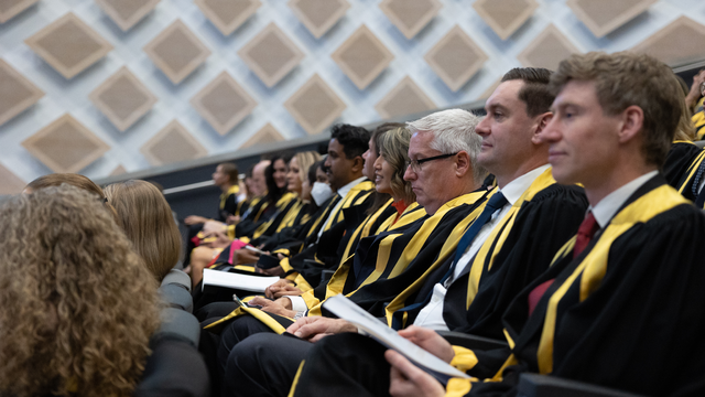 ANZCA fellows sitting in a row in their fellowship gowns with a booklet in their hands