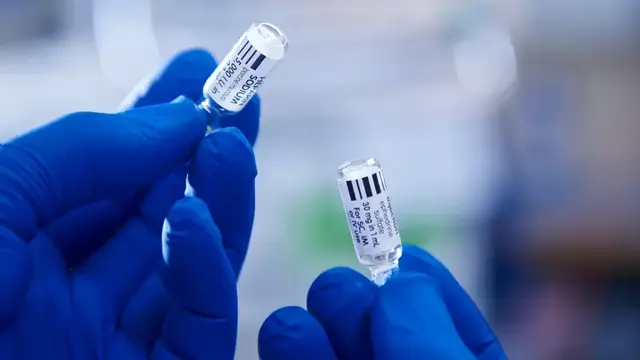 Gloved hands holding up two drug vials 